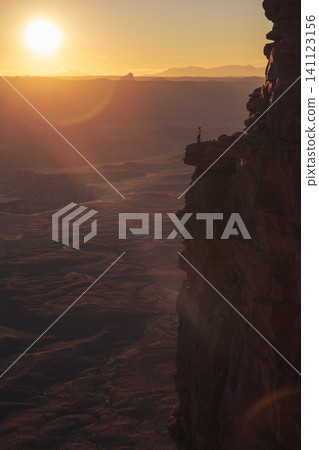 Solitary person stands on rugged cliff edge, observing vibrant orange golden sunset across vast sky and majestic mountain cloudscape in Utah, USA, on thrilling adventure travel Solitary person stands on rugged cliff edge, observing vibrant orange golden sunset across vast sky and majestic mountain cloudscape in Utah, USA, on thrilling adventure travel 141123156