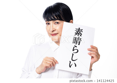 A middle-aged woman in a white shirt smiles, holding a piece of paper with the word "wonderful" written on it in both hands. 141124425