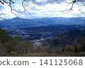 A vast valley landscape viewed from the mountaintop, seen through the branches of bare trees. 141125068