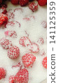 Extreme close-up of vibrant red raspberries scattered on a bed of white granulated sugar, highlighting their texture and seeds. 141125359