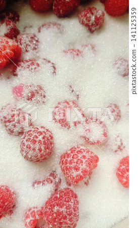 Extreme close-up of vibrant red raspberries scattered on a bed of white granulated sugar, highlighting their texture and seeds. Extreme close-up of vibrant red raspberries scattered on a bed of white granulated sugar, highlighting their texture and seeds. 141125359