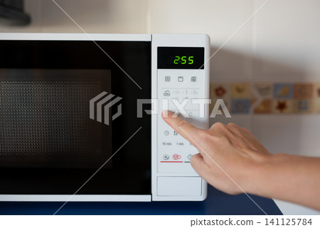 Hand pressing buttons on modern microwave oven with digital display 141125784