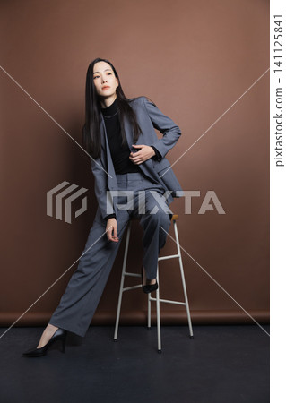 A woman in a suit sitting on a chair 141125841