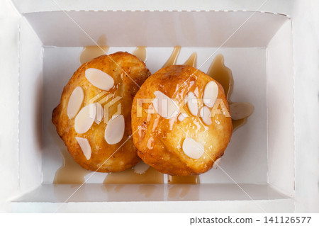 Sweet cottage cheese pancake with syrup and almond flake in white paper take out box top view close up flat lay delicious dessert snack Sweet cottage cheese pancake with syrup and almond flake in white paper take out box top view close up flat lay delicious dessert snack 141126577