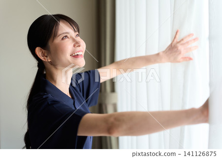 A cleaning lady opens the curtains in the guest room. 141126875