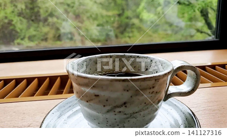 坐在窗邊喝咖啡,欣賞窗外鬱鬱蔥蔥的綠色植物。 坐在窗邊喝咖啡,欣賞窗外鬱鬱蔥蔥的綠色植物。 141127316