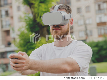 A young man plays a game wearing virtual reality glasses on the street. A young man plays a game wearing virtual reality glasses on the street. 141127442