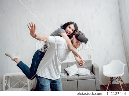 The young man with girlfriend playing games with virtual reality goggles The young man with girlfriend playing games with virtual reality goggles 141127444
