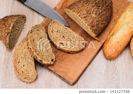 Different breeds on wooden background. Knife on a wooden board with bread and different buns on the table. Crisp bread on a wooden board. Different breeds on wooden background. Knife on a wooden board with bread and different buns on the table. Crisp bread on a wooden board. 141127586