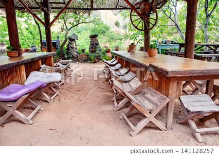 Setting with wooden tables and benches in an outdoor area surrounded by plants and rocks near a farming location Setting with wooden tables and benches in an outdoor area surrounded by plants and rocks near a farming location 141128257