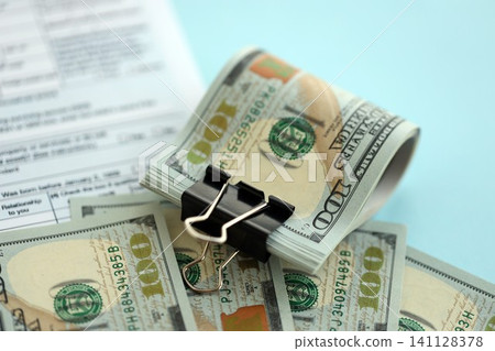 Big amount of United States hundred dollar bills in bunch on table with tax return form Big amount of United States hundred dollar bills in bunch on table with tax return form 141128378