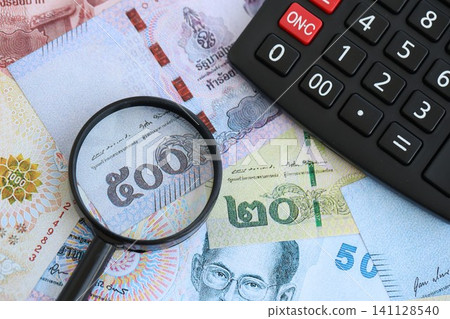 Thai baht currency money bills and calculator with magnifying glass. The concept of taxation Thai baht currency money bills and calculator with magnifying glass. The concept of taxation 141128540
