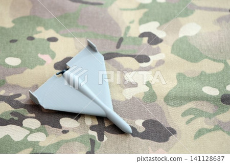 Unnamed grey toy drone model on camouflage fabric. Kamikaze drone for bombing targets Unnamed grey toy drone model on camouflage fabric. Kamikaze drone for bombing targets 141128687