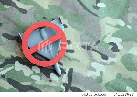 Unnamed grey toy drone and red prohibition sign on camouflage fabric. Anti-aircraft warfare Unnamed grey toy drone and red prohibition sign on camouflage fabric. Anti-aircraft warfare 141128688