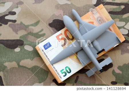 Unnamed grey toy drones and Euro money bills stack on camouflage fabric close up Unnamed grey toy drones and Euro money bills stack on camouflage fabric close up 141128694