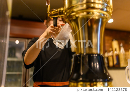 The hands pouring beer into a glass from a beer dispenser. 141128878