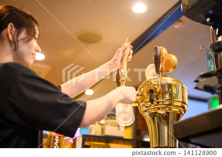 A woman pours beer from a beer tap. 141128900