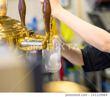 Pour beer from the beer tap into a glass. 141128964