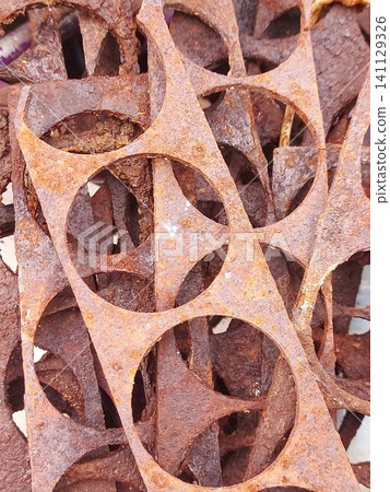 Close-up of rusty metal industrial scraps with circular cutout patterns. Corroded steel texture, abstract geometric shapes, weathered metal background, oxidation, recycling concept, grunge surface Close-up of rusty metal industrial scraps with circular cutout patterns. Corroded steel texture, abstract geometric shapes, weathered metal background, oxidation, recycling concept, grunge surface 141129326