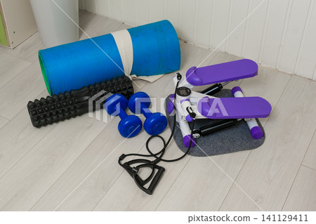 Sport Home exercise equipment. Efficient workout routine. Fitness gear placed for home fit. Yoga mat, roller, dumbbells on room floor ready for recovery session. Personal inventory for weight loss Sport Home exercise equipment. Efficient workout routine. Fitness gear placed for home fit. Yoga mat, roller, dumbbells on room floor ready for recovery session. Personal inventory for weight loss 141129411