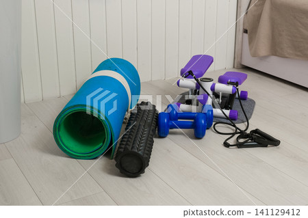 Sport Home exercise equipment. Efficient workout routine. Fitness gear placed for home fit. Yoga mat, roller, dumbbells on room floor ready for recovery session. Personal inventory for weight loss 141129412