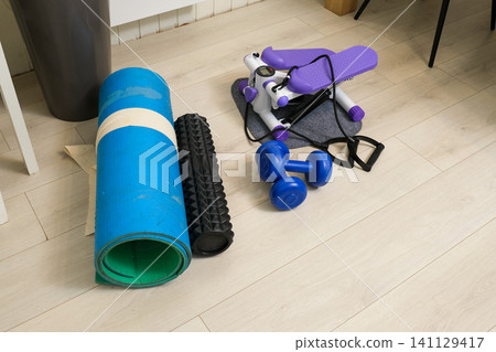 Sport Home exercise equipment. Efficient workout routine. Fitness gear placed for home fit. Yoga mat, roller, dumbbells on room floor ready for recovery session. Personal inventory for weight loss 141129417