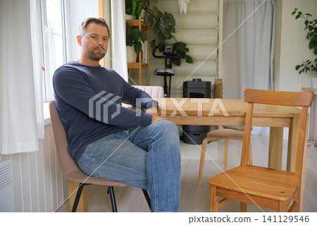 Reflective man relaxes. Middleaged male peacefully sitting inside. Indoor scene tranquil middle aged man dressed casually. Bearded 40s man seated indoors, neutral expression, wood panel background Reflective man relaxes. Middleaged male peacefully sitting inside. Indoor scene tranquil middle aged man dressed casually. Bearded 40s man seated indoors, neutral expression, wood panel background 141129546
