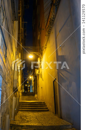 Naples, italy. December 27, 2024. Naples historic center alley with cobblestone steps winding upwards, illuminated by warm streetlights at night, showing urban architecture 141129570