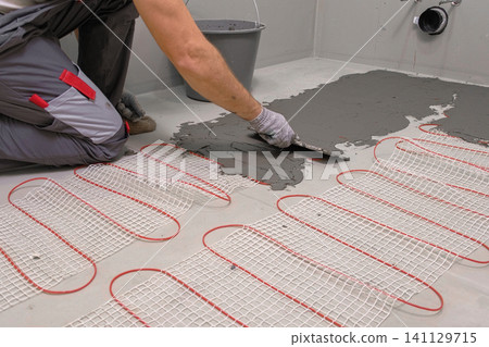 Electric Heating Mat Installing in the Tile Adhesive. Underfloor Dual Core Fiberglass Mesh Mat. Warm Floor Heating System. Warming. Worker Applying Concrete Mortar for Warm Floor. Renovation work. 4K 141129715