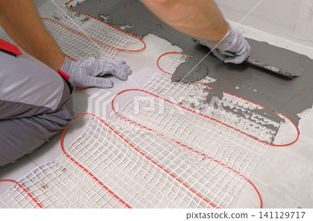 Electric Heating Mat Installing in the Tile Adhesive. Underfloor Dual Core Fiberglass Mesh Mat. Warm Floor Heating System. Warming. Worker Applying Concrete Mortar for Warm Floor. Renovation work. 4K 141129717