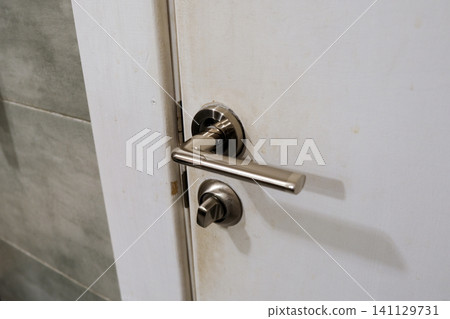 Doorknob. Metal door handle lock and latch of brass on veneer doors. Door wooden half opening through interior bedroom background, selective focus. Modern trends in interior design. Close-up Doorknob. Metal door handle lock and latch of brass on veneer doors. Door wooden half opening through interior bedroom background, selective focus. Modern trends in interior design. Close-up 141129731