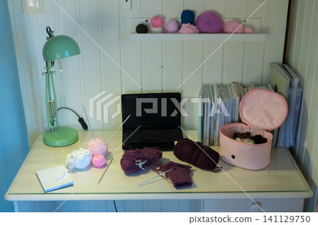 Craft desk displaying an assortment of acrylic yarn, skeins of thread and knitting needles. Laptop and pattern book accessories. Table for crochet learning. DIY workspace. Crafts Hobbies workplace. Craft desk displaying an assortment of acrylic yarn, skeins of thread and knitting needles. Laptop and pattern book accessories. Table for crochet learning. DIY workspace. Crafts Hobbies workplace. 141129750