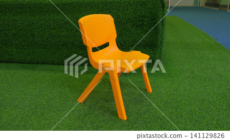 Colorful plastic kids chair. Orange children's chair in child room. Space for text. Stool for children in bright vivid playroom. Furniture for baby toddlers. Kindergarten preschool classroom concept Colorful plastic kids chair. Orange children's chair in child room. Space for text. Stool for children in bright vivid playroom. Furniture for baby toddlers. Kindergarten preschool classroom concept 141129826