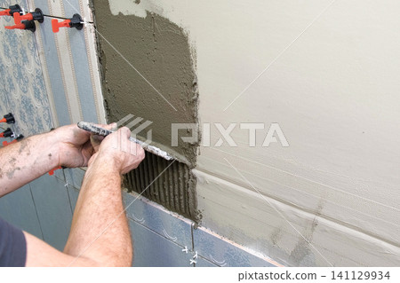 Worker Laying Ceramic Tiles on the Wall. Repairman Placing White Gray Square Tiles, Applying Adhesive. Builder Installing Tile Using Leveler, Tile Leveling Clips. Tiling. Finishing Repair Work. 4K Worker Laying Ceramic Tiles on the Wall. Repairman Placing White Gray Square Tiles, Applying Adhesive. Builder Installing Tile Using Leveler, Tile Leveling Clips. Tiling. Finishing Repair Work. 4K 141129934