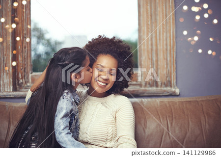 Mother, child and kiss cheek on couch in home for weekend relaxing or holiday bonding, love or support. Woman, daughter and connection in apartment living room for vacation care, youth or parenting Mother, child and kiss cheek on couch in home for weekend relaxing or holiday bonding, love or support. Woman, daughter and connection in apartment living room for vacation care, youth or parenting 141129986