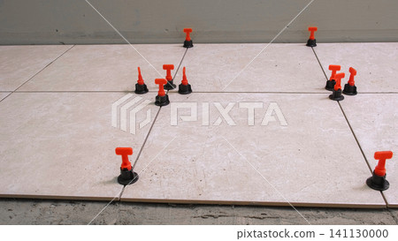 Worker Hand Laying Ceramic Tiles on the Floor. Repairman Placing White Gray Square Tiles, Applying Adhesive. Builder Installing Tile Using Leveler, Tile Leveling Clips. Tiling. Finishing Repair Work. Worker Hand Laying Ceramic Tiles on the Floor. Repairman Placing White Gray Square Tiles, Applying Adhesive. Builder Installing Tile Using Leveler, Tile Leveling Clips. Tiling. Finishing Repair Work. 141130000