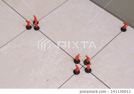 Worker Hand Laying Ceramic Tiles on the Floor. Repairman Placing White Gray Square Tiles, Applying Adhesive. Builder Installing Tile Using Leveler, Tile Leveling Clips. Tiling. Finishing Repair Work. Worker Hand Laying Ceramic Tiles on the Floor. Repairman Placing White Gray Square Tiles, Applying Adhesive. Builder Installing Tile Using Leveler, Tile Leveling Clips. Tiling. Finishing Repair Work. 141130011