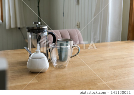 Wooden table with French press, glass cup, ceramic sugar jar, soft natural light, shallow depth of field. Warm cozy Minimalist kitchen beverage setting. Morning coffee accessories in natural light. Wooden table with French press, glass cup, ceramic sugar jar, soft natural light, shallow depth of field. Warm cozy Minimalist kitchen beverage setting. Morning coffee accessories in natural light. 141130031