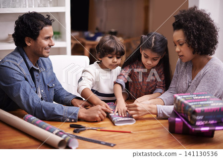 Parents, kids and table with wrapping gift or presents for Christmas season with smile, support and bonding. Home, family and happy together in living room for child development, growth and memories Parents, kids and table with wrapping gift or presents for Christmas season with smile, support and bonding. Home, family and happy together in living room for child development, growth and memories 141130536