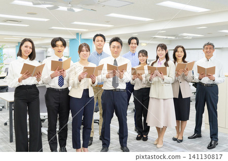 Participants in the employee training line up in the office, smiling and holding booklets. 141130817