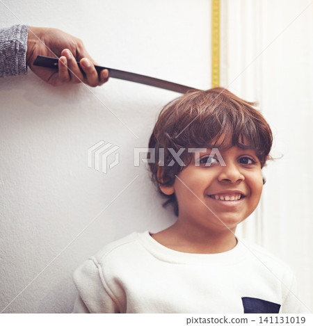 Child, portrait and height measure at wall for growth development in home with ruler, tape or smile. Boy, face and hand with marking for childhood chart in home for checking size, tall or happiness Child, portrait and height measure at wall for growth development in home with ruler, tape or smile. Boy, face and hand with marking for childhood chart in home for checking size, tall or happiness 141131019