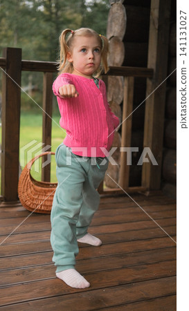 Little 5 years old kid girl practicing punches, karate, taekwondo movements at home. Athlete child practicing martial arts outdoors. Training in autumn day. Nature background. Dynamic Kyungkido. Little 5 years old kid girl practicing punches, karate, taekwondo movements at home. Athlete child practicing martial arts outdoors. Training in autumn day. Nature background. Dynamic Kyungkido. 141131027