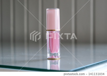 Lipstick on neutral interior background. Liquid lip stick clear tube. Makeup cosmetic product. Front view copy space. Shimmer Pink lip gloss for makeup creating beauty and shine. Glamour modern design Lipstick on neutral interior background. Liquid lip stick clear tube. Makeup cosmetic product. Front view copy space. Shimmer Pink lip gloss for makeup creating beauty and shine. Glamour modern design 141131034