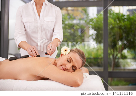 Woman, hands and hot stone massage at spa with masseuse, flower for natural treatment and wellness with zen. Calm, peace and luxury bodycare with warm rocks for detox, self care and holistic healing 141131116