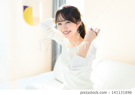 A young woman sitting on a sofa tying her hair A young woman sitting on a sofa tying her hair 141131896