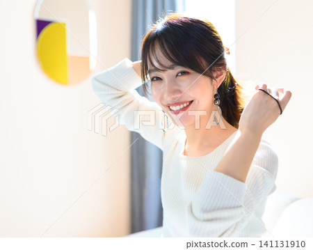 一位年輕女子坐在沙發上綁頭髮。 141131910