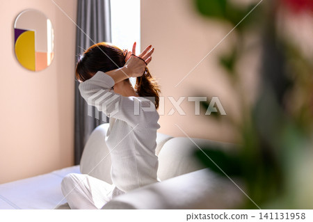 A woman tying her hair in her room 141131958