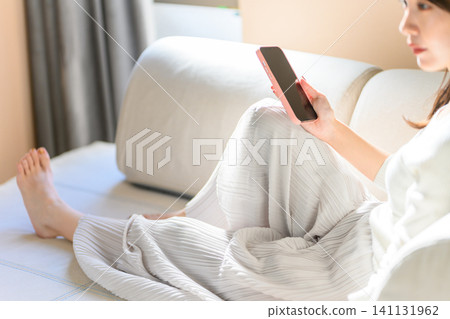 A woman operating a smartphone on the sofa A woman operating a smartphone on the sofa 141131962