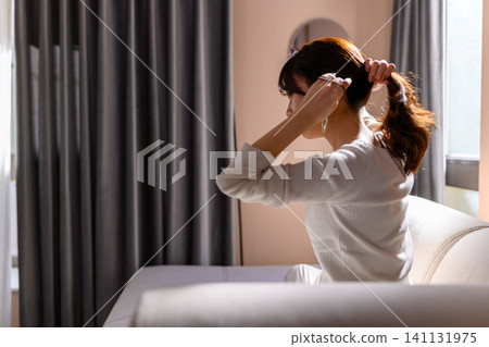 A woman tying her hair in her room A woman tying her hair in her room 141131975