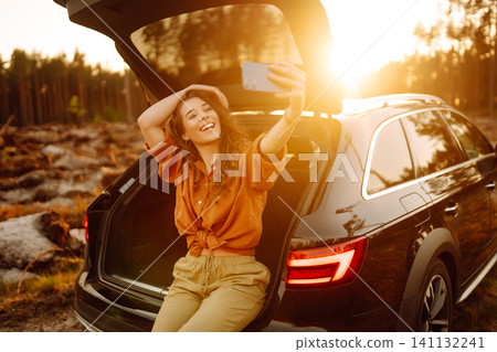 Woman is resting in trunk of car with phone. Concept of traveling by car, active lifestyle. Woman is resting in trunk of car with phone. Concept of traveling by car, active lifestyle. 141132241